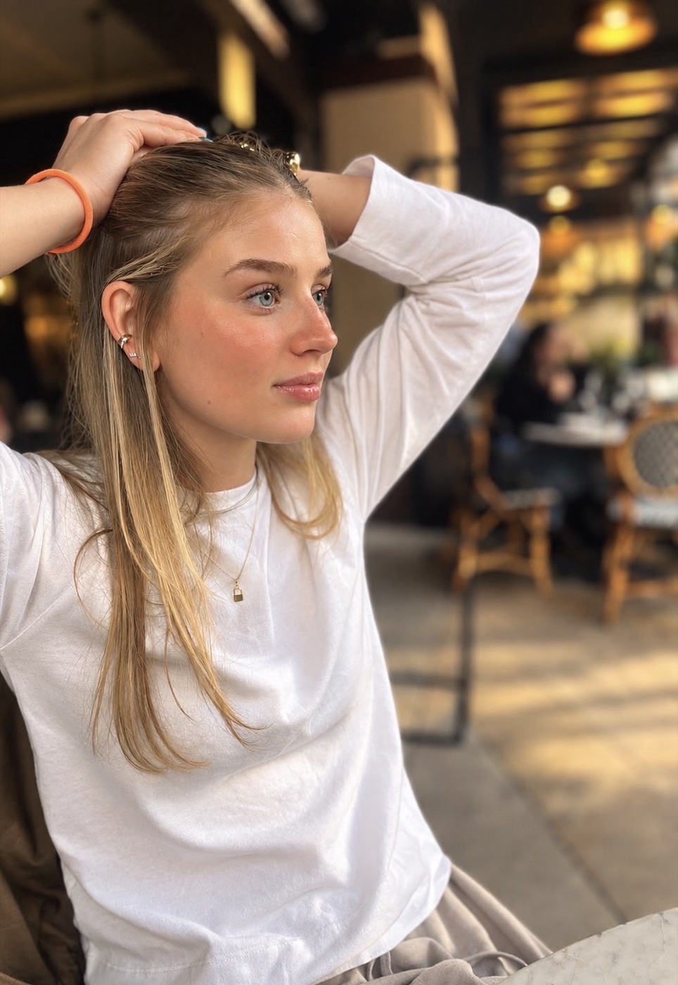 Rachel in a white top, hand in her hair, at a café table